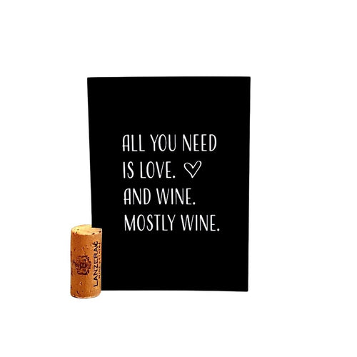 Zwarte kaart voor wijnliefhebbers met in het wit de tekst All You Need Is Love. And Wine. Mostly Wine. Inclusief originele kaartsteun van kurk. Verkrijgbaar bij Wijnstory